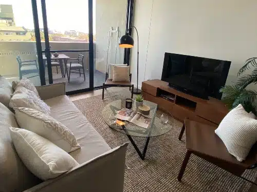 Bright living room with balcony, sofa, TV, and stylish decor in Redfern Apartments.